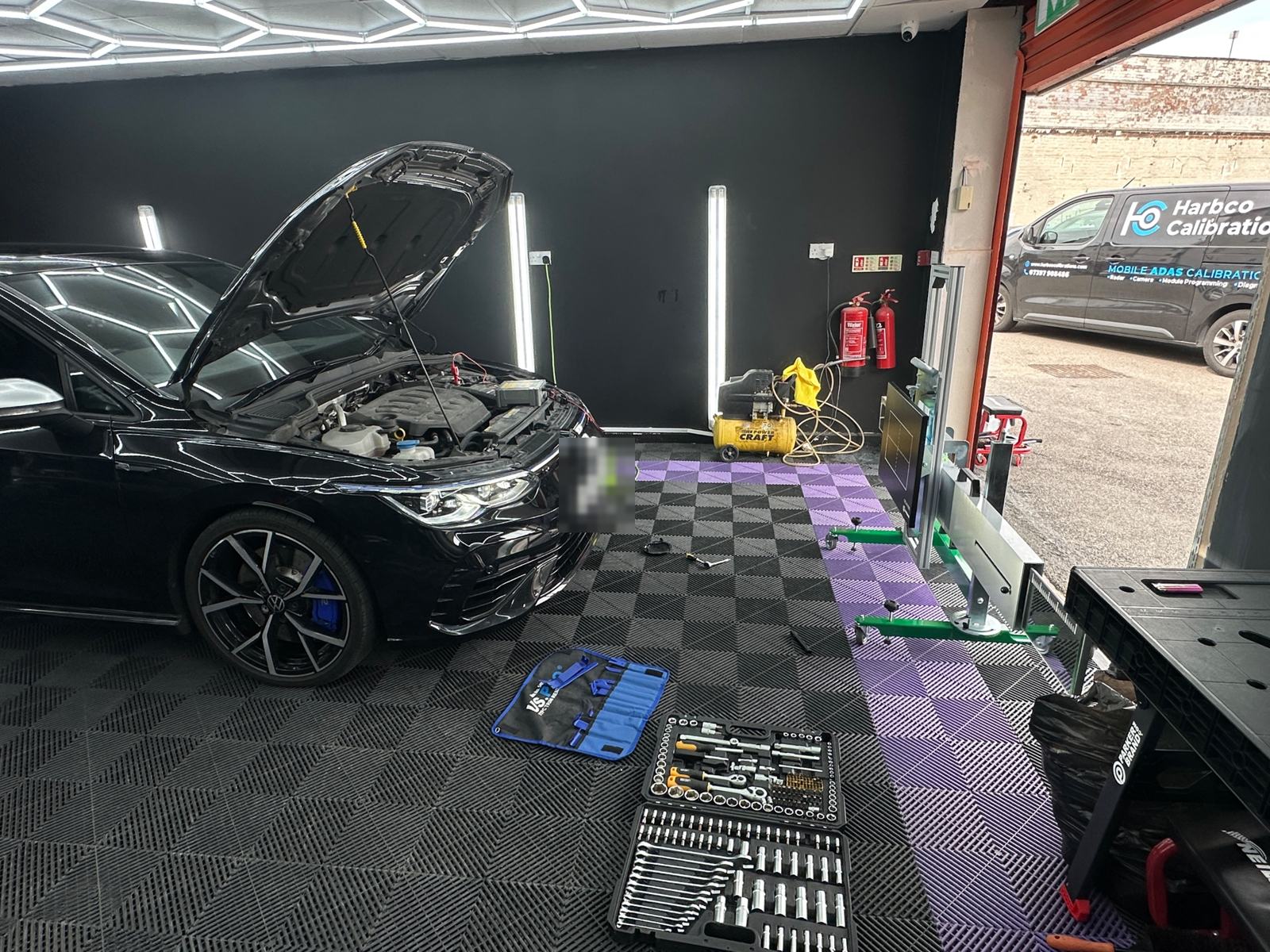 VW Golf with the bonnet up in a calibration bay, radar rig in front and the Harbco van outside in Leeds
