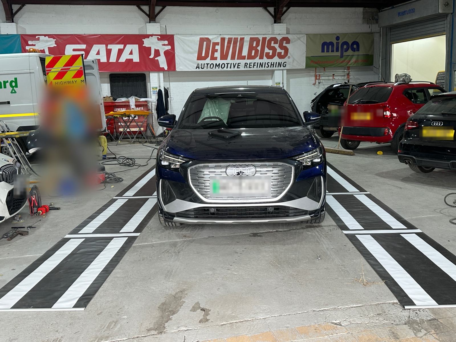 Audi Q4 e-tron centred between striped surround-view calibration mats in a bodyshop in Sheffield